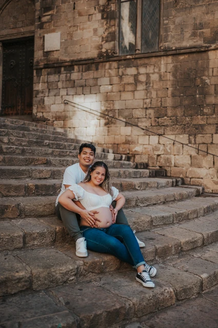 A seated portrait on the stone steps | Barcelona maternity photoshoot The couple sitting close together on the stone steps and smiling towards the camera during their maternity photoshoot in Barcelona.