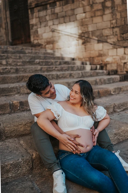 A quiet moment on the stone steps | Barcelona maternity photoshoot The couple sitting together on the stone steps with their hands resting on her bump during their maternity photoshoot in Barcelona.