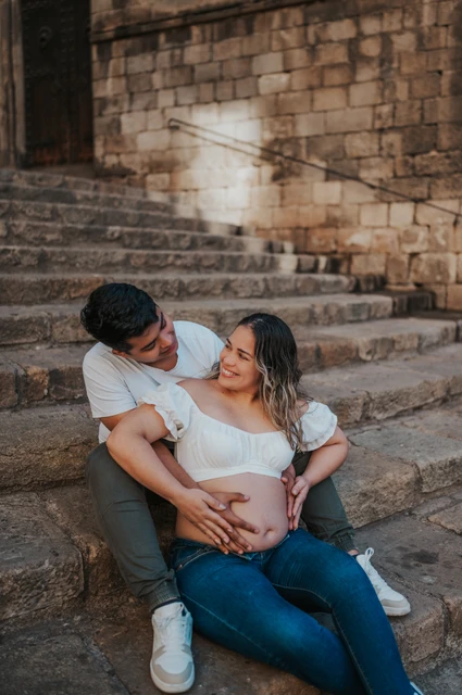 A quiet moment on the stone steps | Barcelona maternity photoshoot The couple sitting together on the stone steps with their hands resting on her bump during their maternity photoshoot in Barcelona.