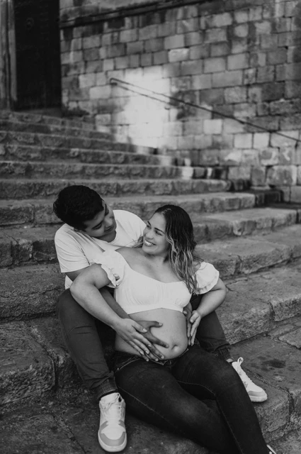 A quiet moment on the stone steps in black and white | Barcelona maternity photoshoot Black-and-white photograph: the couple sitting together on the stone steps with their hands resting on her bump during their maternity photoshoot in Barcelona.