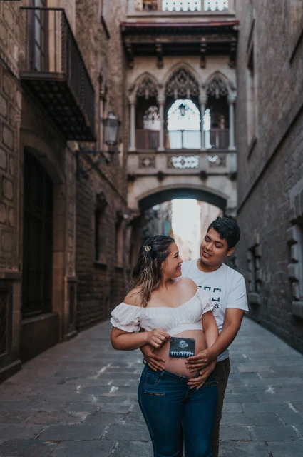 Their ultrasound photograph beneath the bridge | Barcelona maternity photoshoot The couple holding an ultrasound photograph together beneath the ornate bridge between the buildings during their maternity photoshoot in Barcelona.