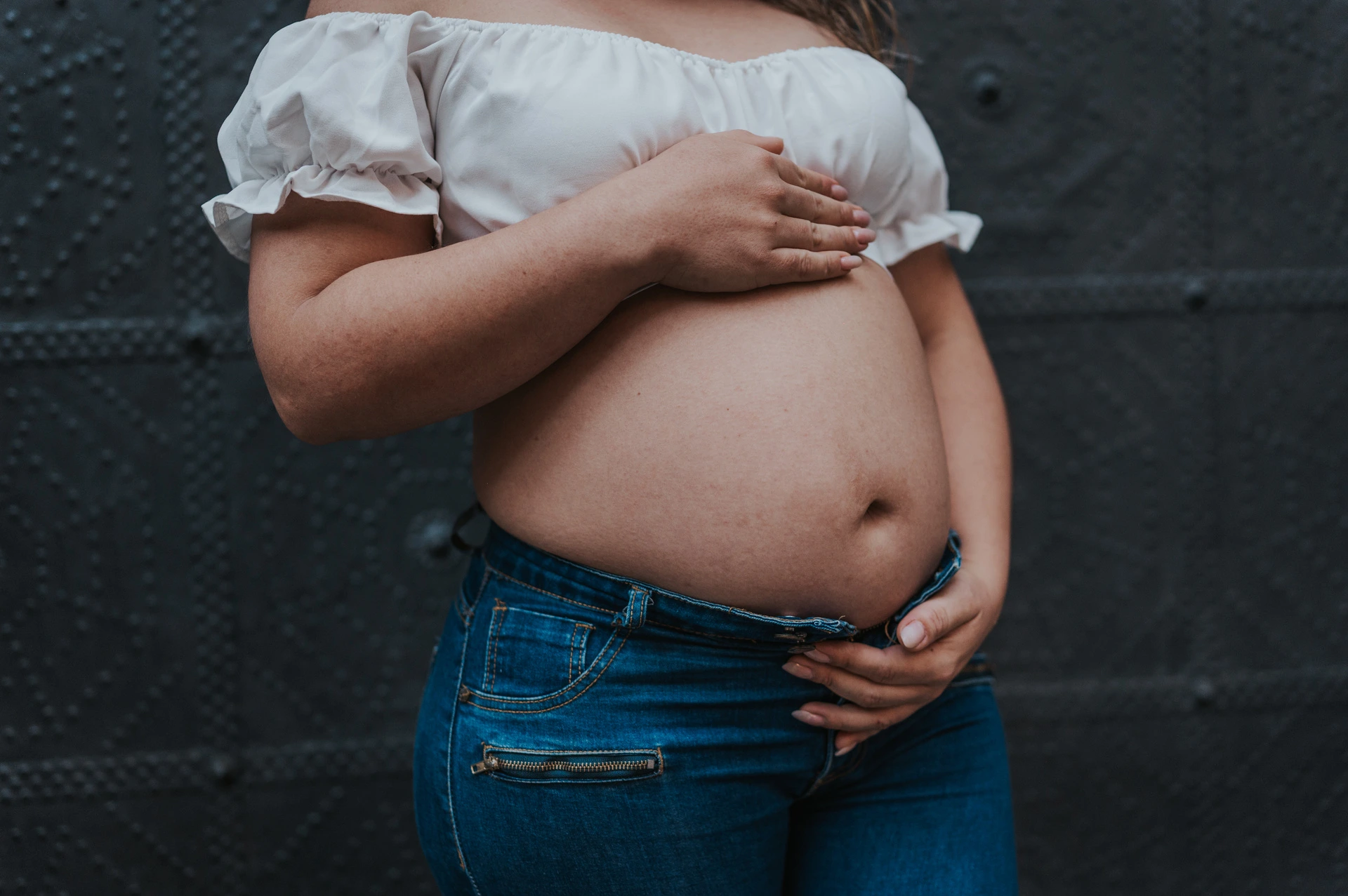 A close view of the mother-to-be’s hands resting on her bump against a dark door during their maternity photoshoot in Barcelona.