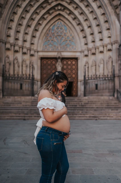 A maternity portrait beside the cathedral | Barcelona maternity photoshoot The mother-to-be standing sideways with her hands on her bump in front of the cathedral entrance during their maternity photoshoot in Barcelona.