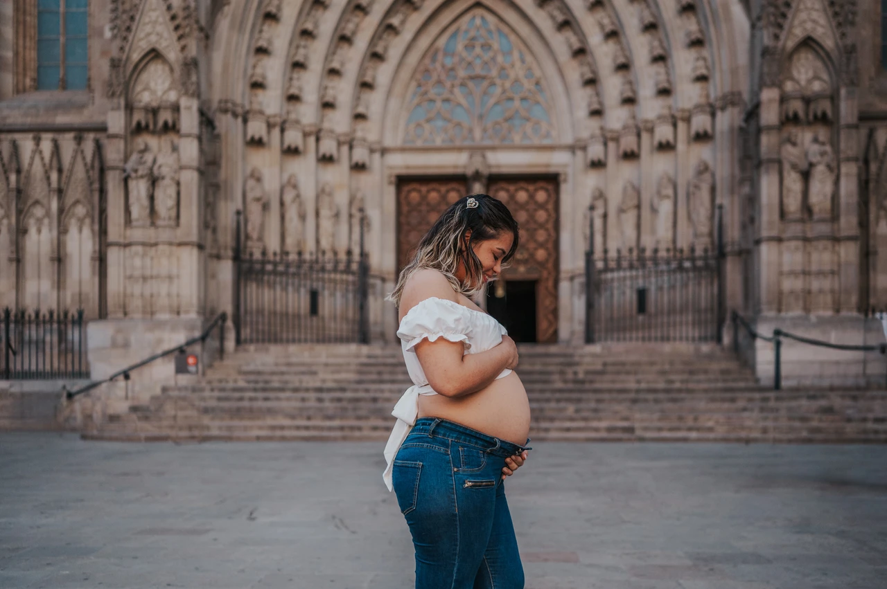 A maternity portrait beside the cathedral | Barcelona maternity photoshoot The mother-to-be standing sideways with her hands on her bump in front of the cathedral entrance during their maternity photoshoot in Barcelona.