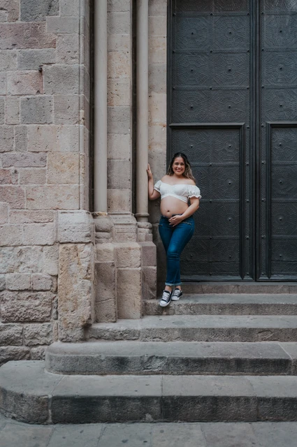A maternity portrait beside the stone doorway | Barcelona maternity photoshoot The mother-to-be holding her bump beside the large doorway and stone steps during their maternity photoshoot in Barcelona.