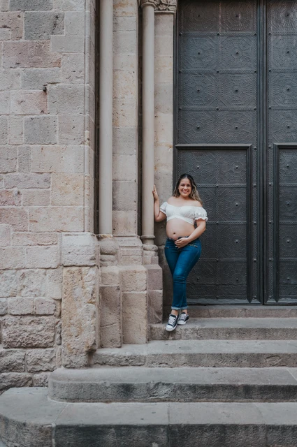A maternity portrait beside the stone doorway | Barcelona maternity photoshoot The mother-to-be holding her bump beside the large doorway and stone steps during their maternity photoshoot in Barcelona.