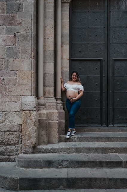 A maternity portrait beside the stone doorway | Barcelona maternity photoshoot The mother-to-be holding her bump beside the large doorway and stone steps during their maternity photoshoot in Barcelona.