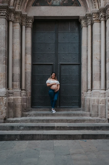 A maternity portrait beside the stone doorway | Barcelona maternity photoshoot The mother-to-be holding her bump beside the large doorway and stone steps during their maternity photoshoot in Barcelona.