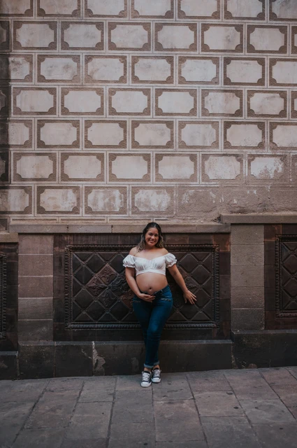 A maternity portrait beside the patterned wall | Barcelona maternity photoshoot The mother-to-be standing beside a patterned wall with her hand resting on her bump during their maternity photoshoot in Barcelona.