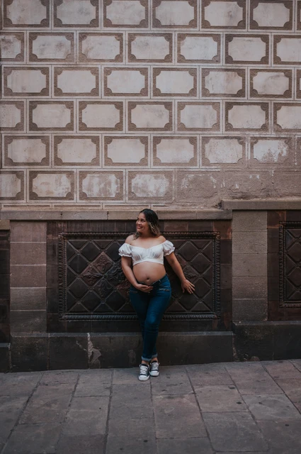 A maternity portrait beside the patterned wall | Barcelona maternity photoshoot The mother-to-be standing beside a patterned wall with her hand resting on her bump during their maternity photoshoot in Barcelona.