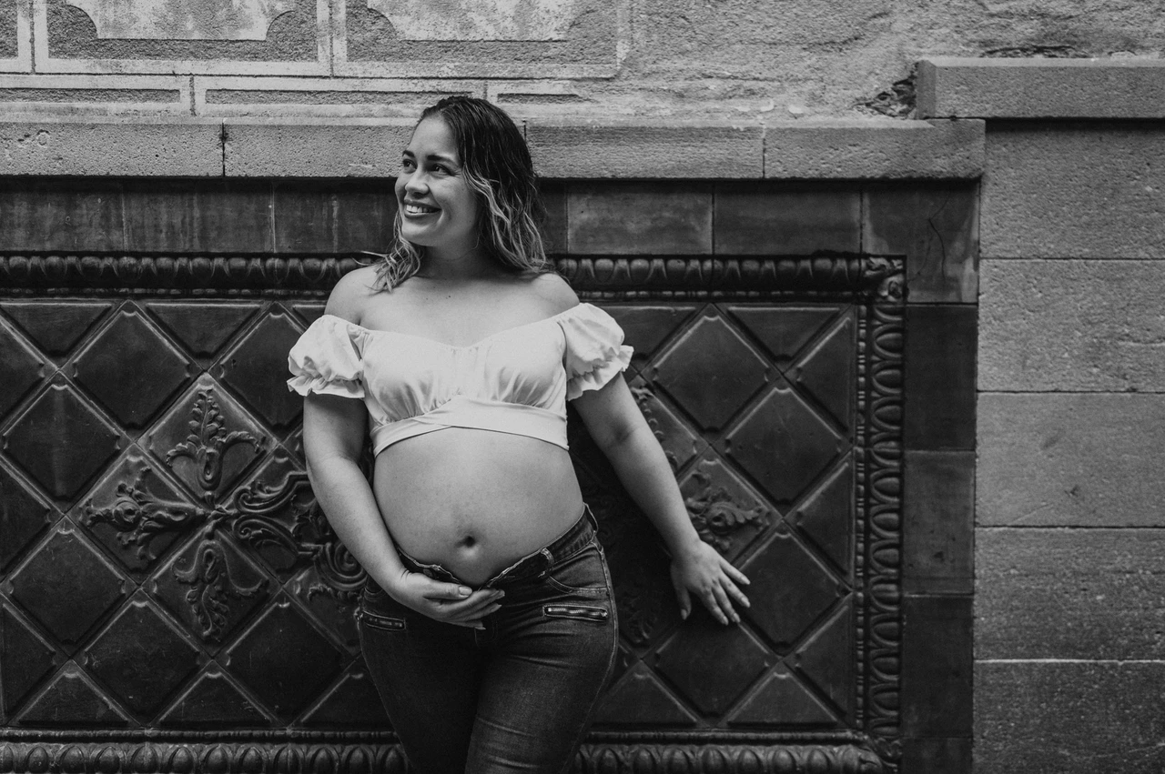 A maternity portrait beside the patterned wall in black and white | Barcelona maternity photoshoot Black-and-white photograph: the mother-to-be standing beside a patterned wall with her hand resting on her bump during their maternity photoshoot in Barcelona.