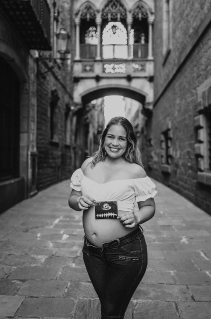 A maternity portrait with their ultrasound photograph in black and white | Barcelona maternity photoshoot Black-and-white photograph: the mother-to-be holding an ultrasound photograph in front of her bump beneath the ornate bridge during their maternity photoshoot in Barcelona.