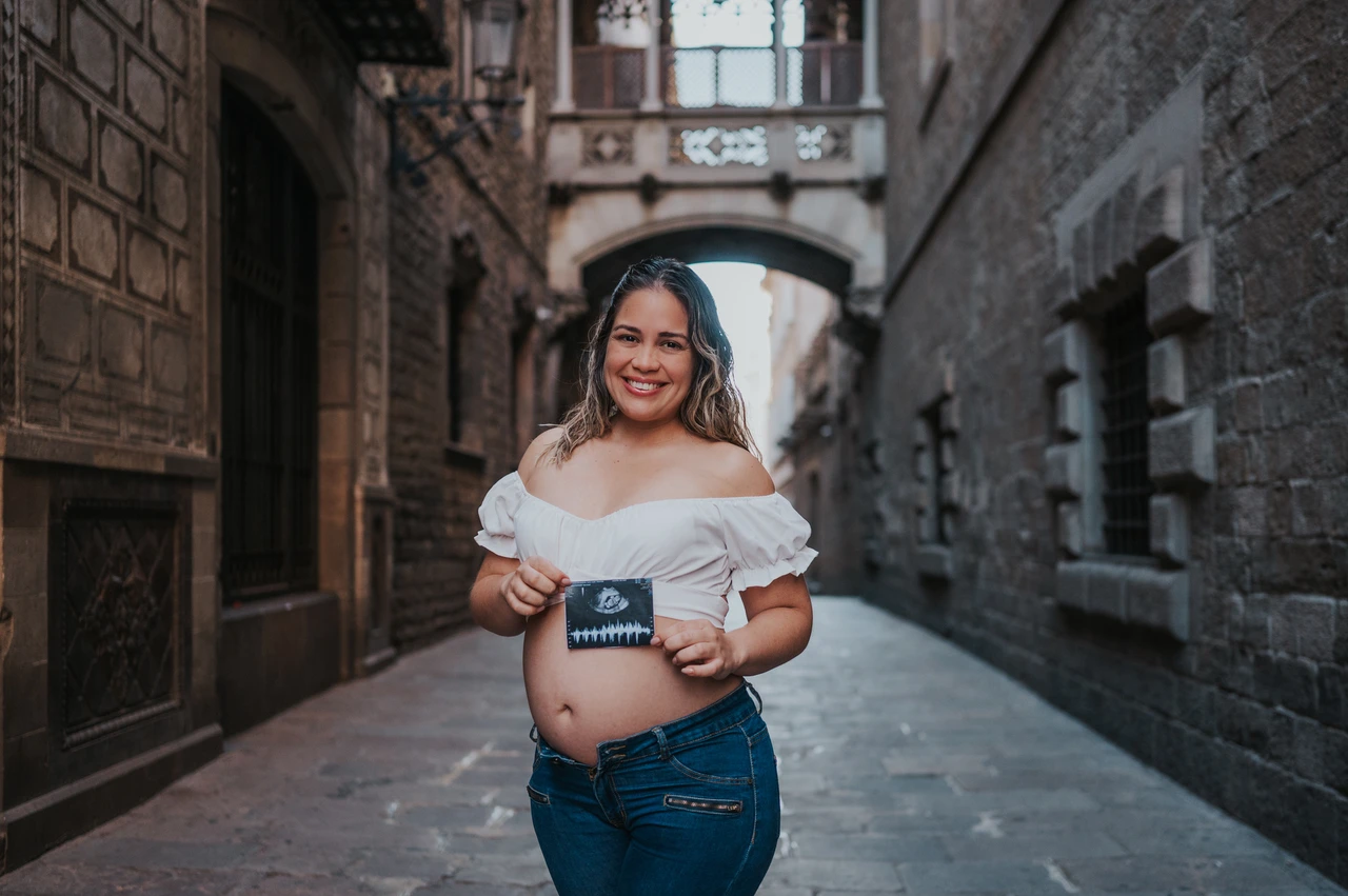 A maternity portrait with their ultrasound photograph | Barcelona maternity photoshoot The mother-to-be holding an ultrasound photograph in front of her bump beneath the ornate bridge during their maternity photoshoot in Barcelona.