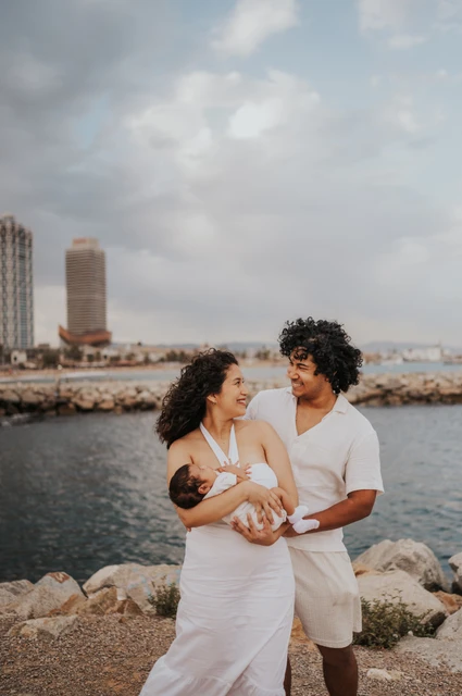 A family portrait with the city behind them | Barcelona newborn family photoshoot The mother holding the newborn with the father close behind and the city across the water during their newborn family photoshoot in Barcelona.