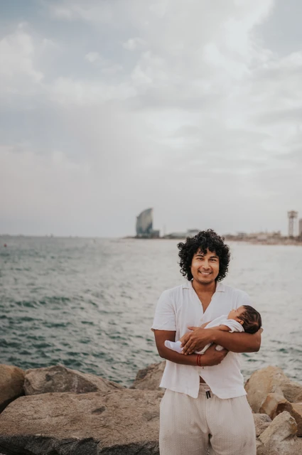 Father and newborn beside the water | Barcelona newborn family photoshoot The father holding his newborn with the water and city behind him during their newborn family photoshoot in Barcelona.