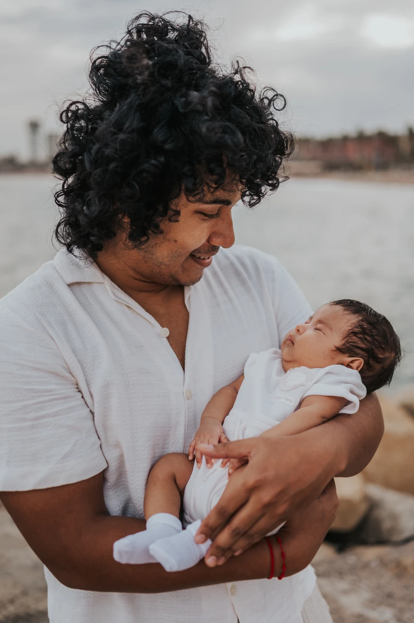 Father and newborn beside the water | Barcelona newborn family photoshoot The father holding his newborn with the water and city behind him during their newborn family photoshoot in Barcelona.