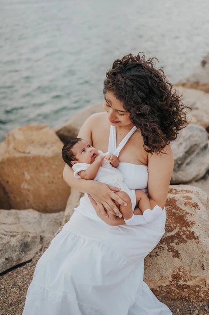 The mother looking down at her newborn while seated on the rocks during their newborn family photoshoot in Barcelona.