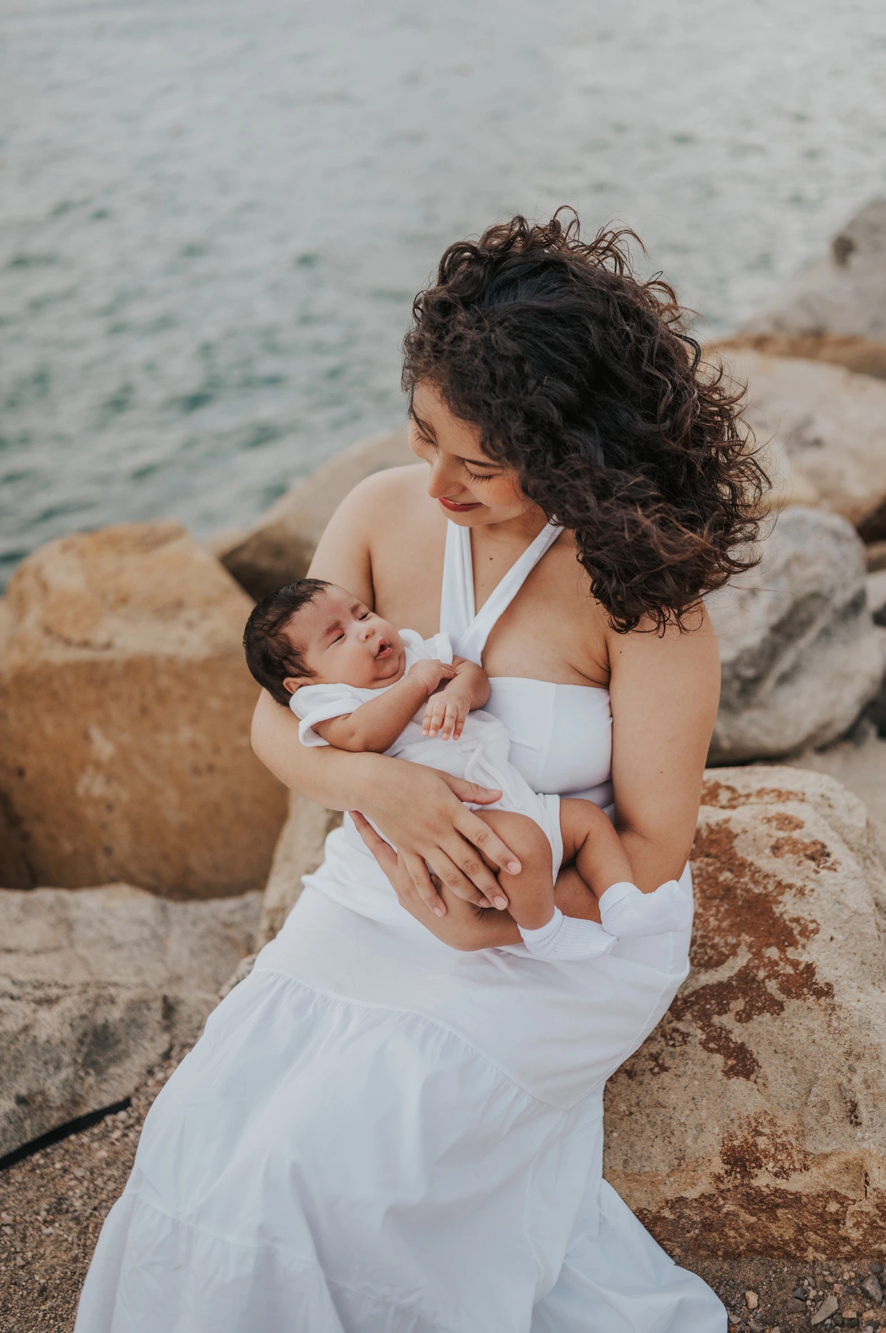 The mother looking down at her newborn while seated on the rocks during their newborn family photoshoot in Barcelona.