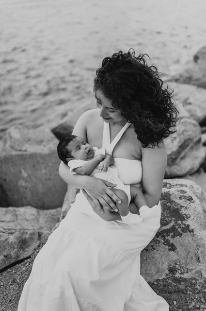 A quiet moment with her newborn in black and white | Barcelona newborn family photoshoot Black-and-white photograph: the mother looking down at her newborn while seated on the rocks during their newborn family photoshoot in Barcelona.