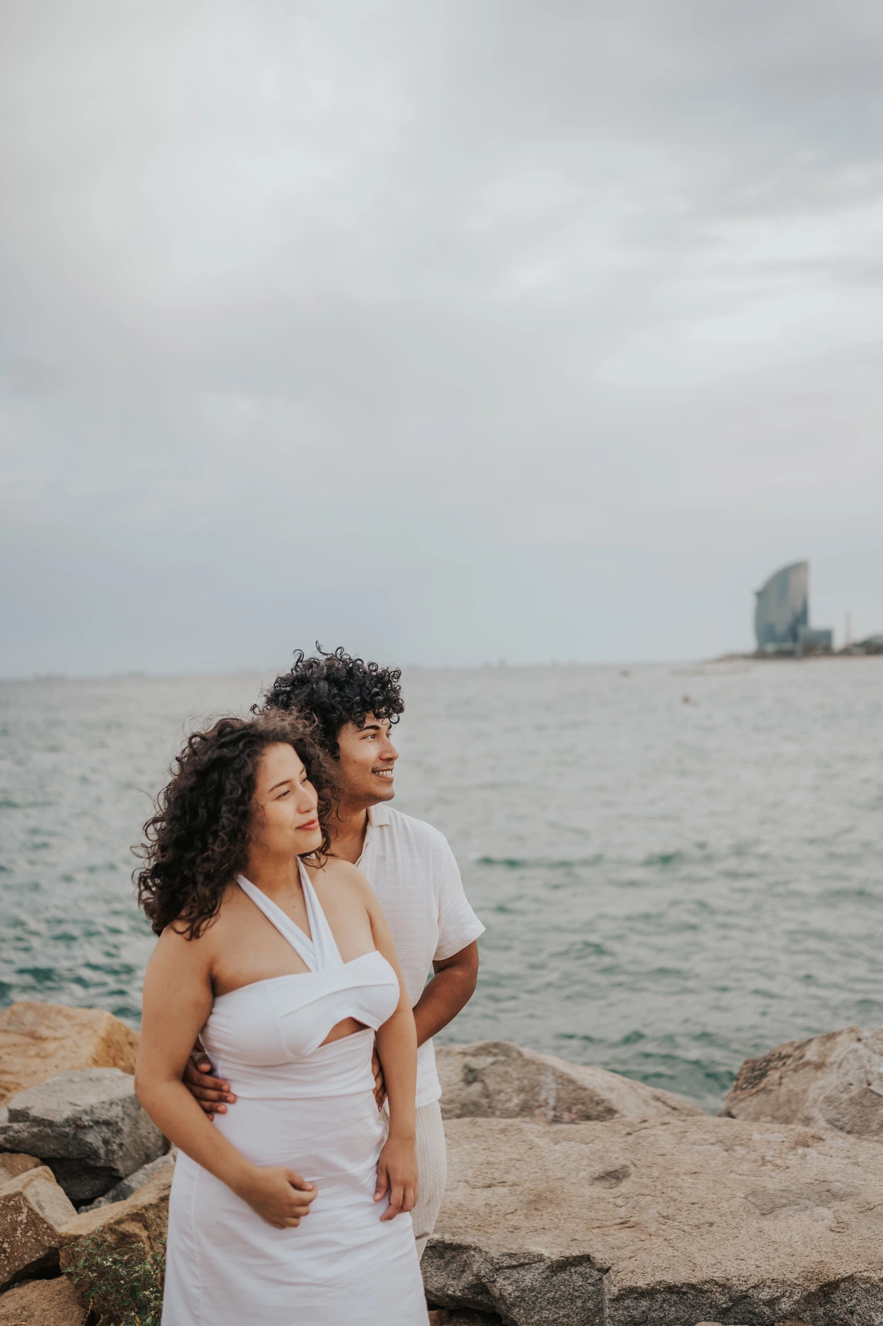 The parents standing close together beside the water during their newborn family photoshoot in Barcelona.