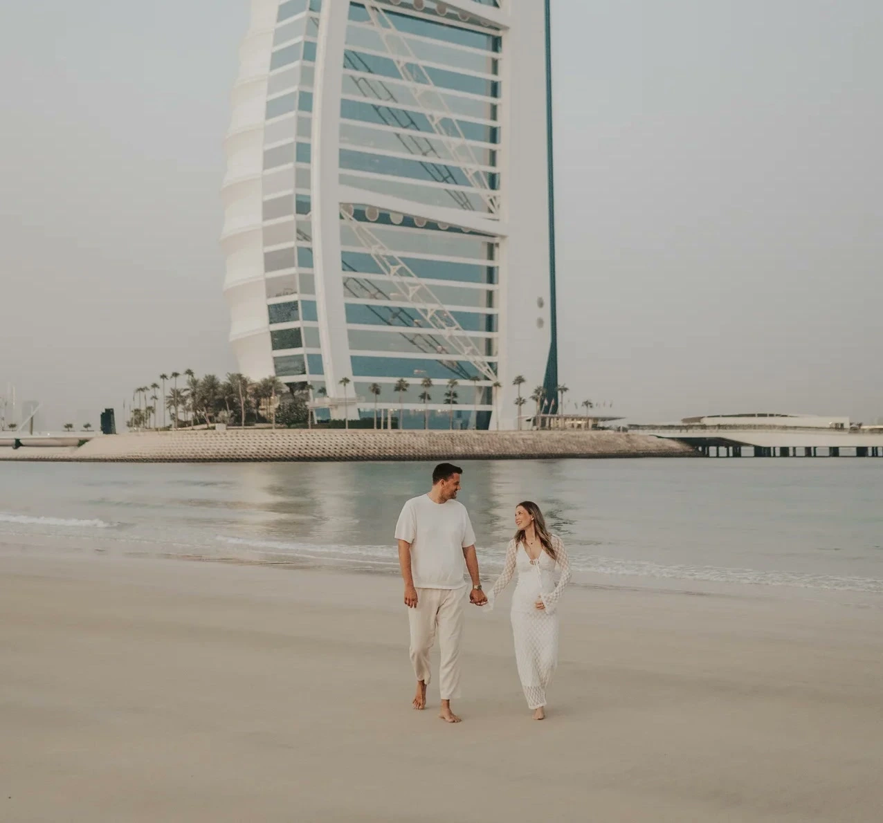 A couple on Dubai beach with Burj Al Arab in the background, framed to keep full subjects visible.