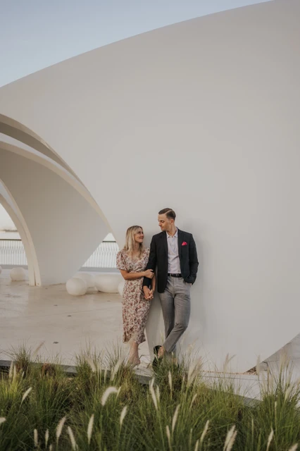 A couple stands together by a modern white architectural structure in Dubai during a city-style photoshoot.