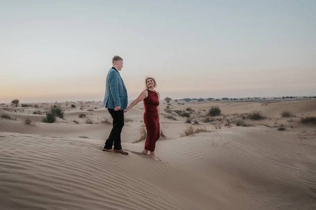 Best couple photoshoot locations Dubai - Wide desert walking portrait A couple walks across open Dubai desert dunes at sunset during a cinematic couple photoshoot.