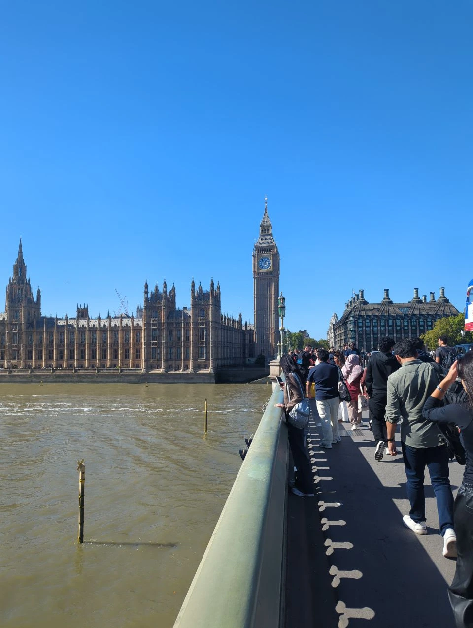 Visitors walking beside the green railing on Westminster Bridge, with Elizabeth Tower and the Palace of Westminster ahead