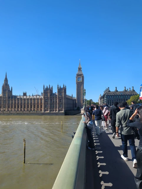 Visitors walking beside the green railing on Westminster Bridge, with Elizabeth Tower and the Palace of Westminster ahead