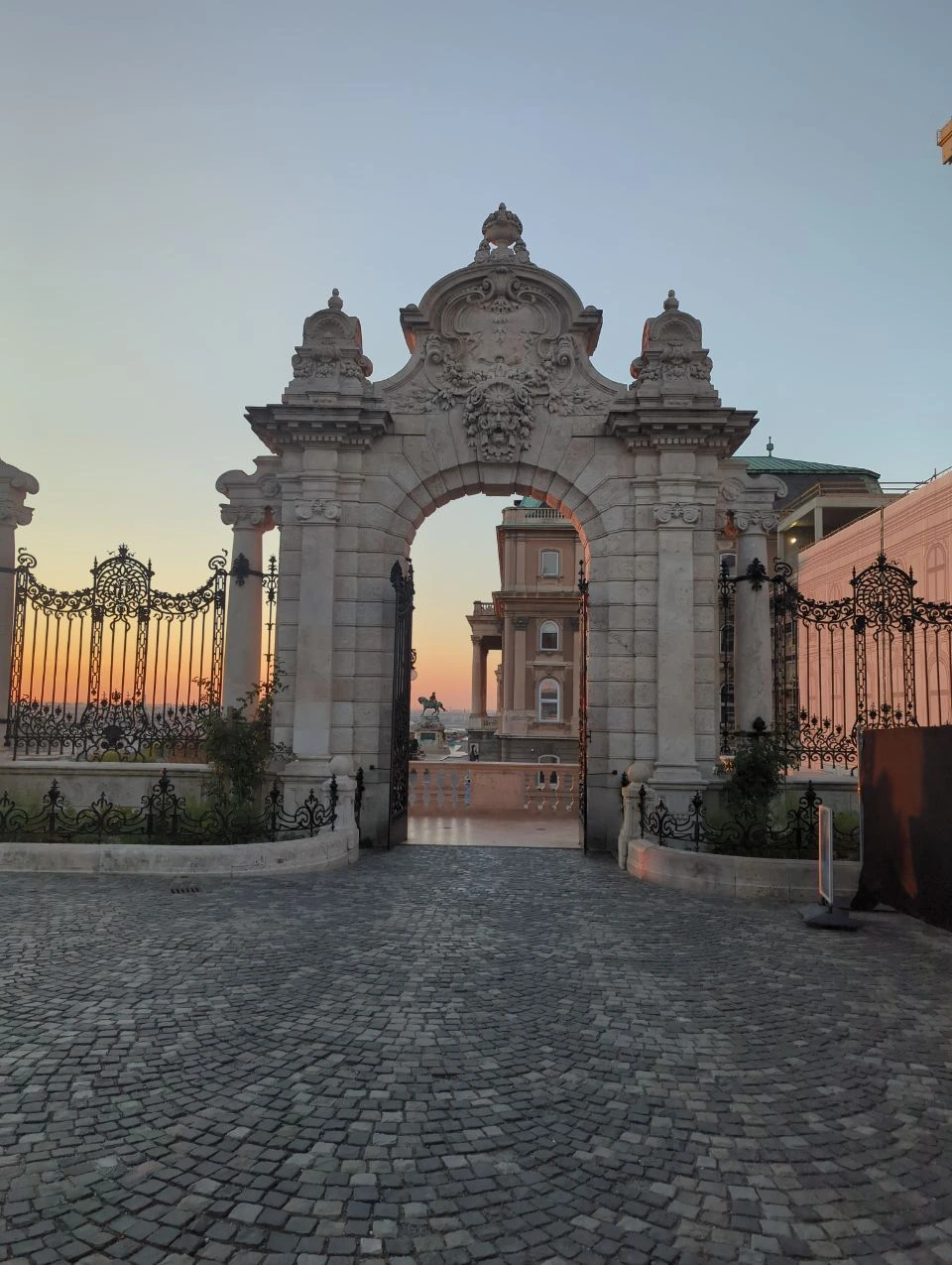 Buda Castle gateway and palace terraces at dawn Ornate stone gateway at Buda Castle with palace balconies and equestrian statue beyond