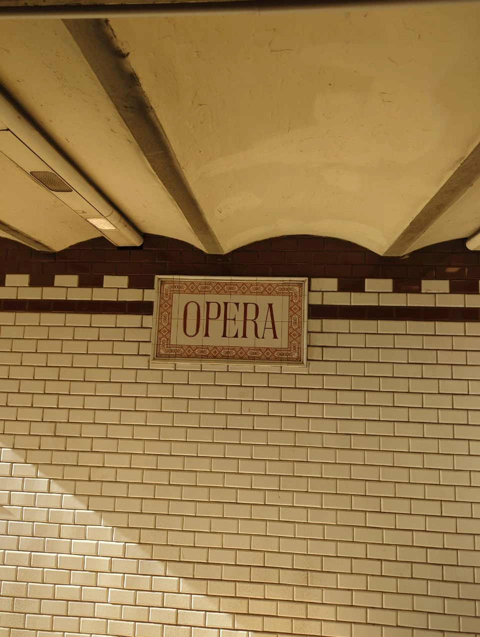Ceramic Opera station name on a white-and-brown tiled wall