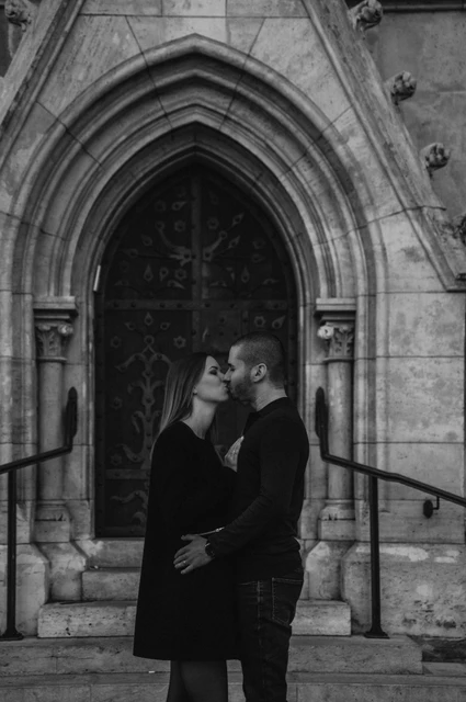 A doorway embrace in black and white at a Budapest couple photoshoot Black-and-white portrait of the couple embracing in front of a carved wooden church door near Fisherman’s Bastion during their couple photoshoot in Budapest.