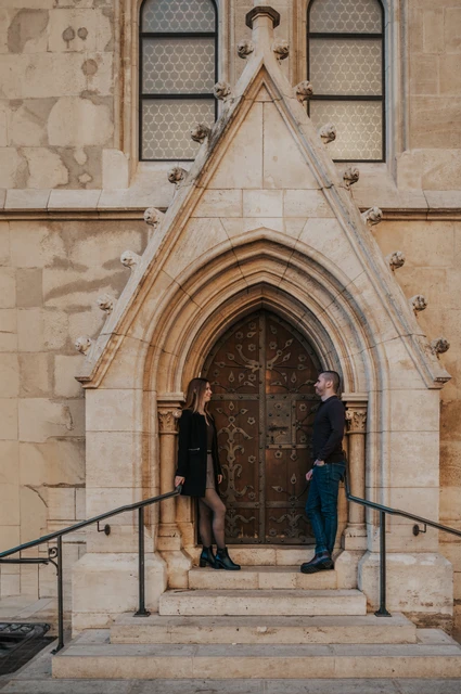 A beautiful pointed stone doorway at a Budapest couple photoshoot The couple standing on either side of a pointed carved doorway in a pale stone church façade near Fisherman’s Bastion during their couple photoshoot in Budapest.