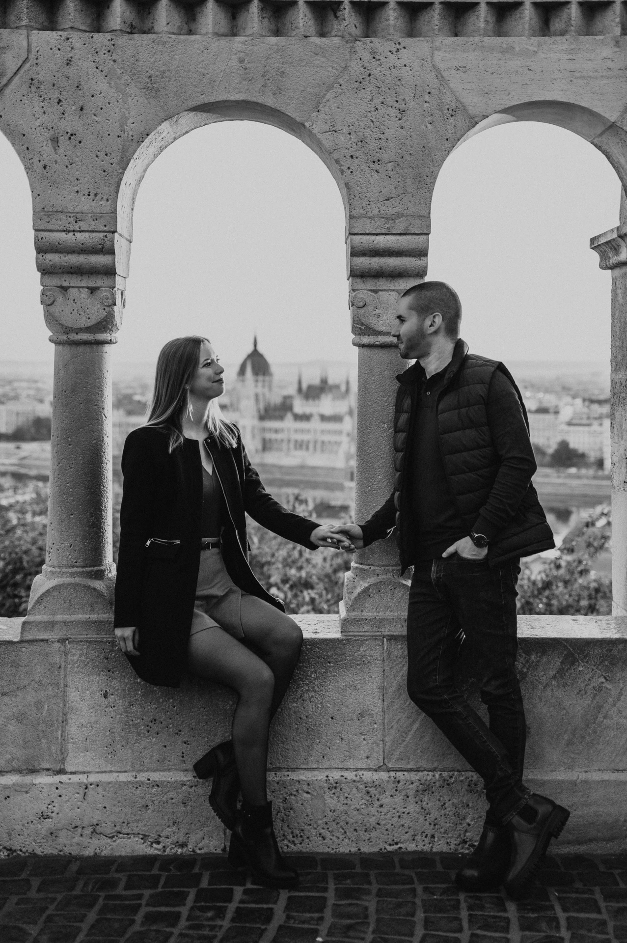 Black-and-white portrait of the couple holding hands beneath Fisherman’s Bastion’s stone arches during their couple photoshoot in Budapest.