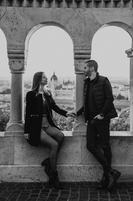 A portrait beneath the arches in black and white at a Budapest couple photoshoot Black-and-white portrait of the couple holding hands beneath Fisherman’s Bastion’s stone arches during their couple photoshoot in Budapest.