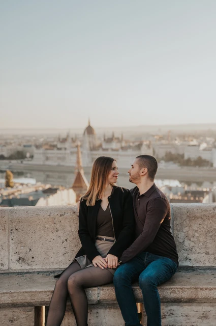 A close bench portrait above Budapest at a Budapest couple photoshoot A closer portrait of the couple holding hands on a stone bench with Budapest’s skyline beyond Fisherman’s Bastion during their couple photoshoot in Budapest.