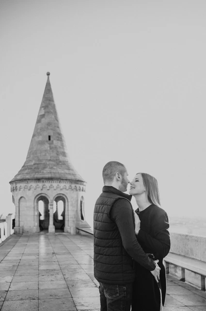 A tower portrait in black and white at a Budapest couple photoshoot Black-and-white portrait of the couple embracing beside Fisherman’s Bastion’s pointed stone tower during their couple photoshoot in Budapest.