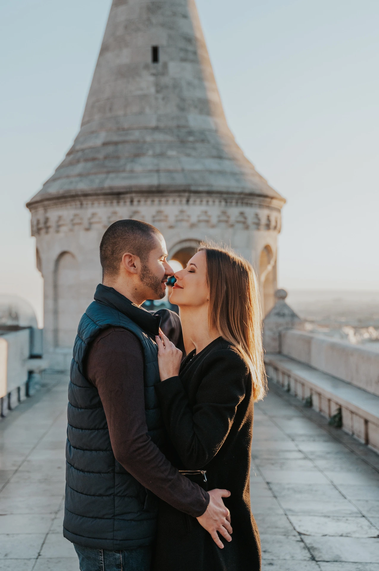 A close portrait of the couple leaning towards one another beneath a pointed tower at Fisherman’s Bastion during their couple photoshoot in Budapest.