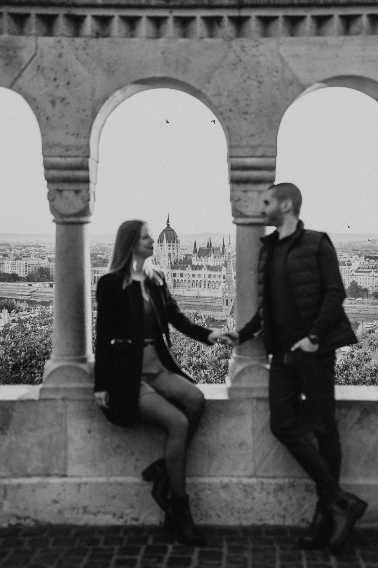 A softly focused black-and-white portrait of the couple holding hands beside the stone columns at Fisherman’s Bastion during their couple photoshoot in Budapest.