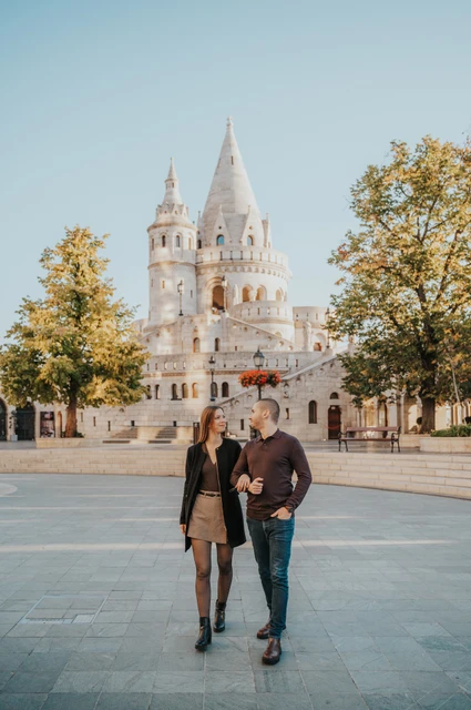 Walking together beside the Bastion at a Budapest couple photoshoot A closer portrait of the couple walking arm in arm with Fisherman’s Bastion’s pale stone towers behind them during their couple photoshoot in Budapest.