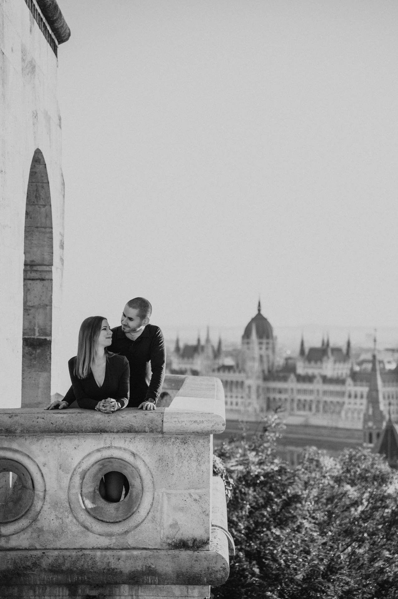 Black-and-white portrait of the couple standing close behind the carved balcony at Fisherman’s Bastion during their couple photoshoot in Budapest.