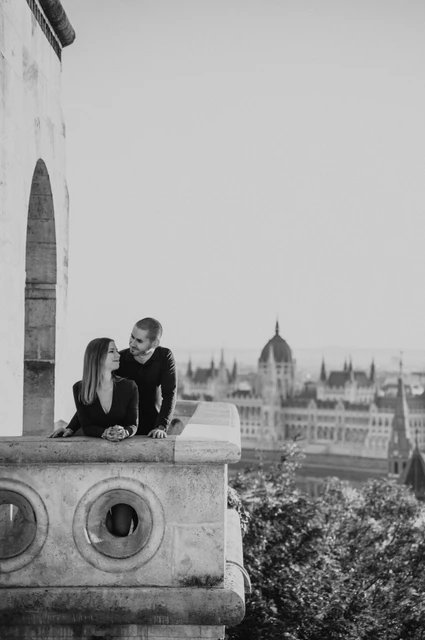 A carved balcony portrait in black and white at a Budapest couple photoshoot Black-and-white portrait of the couple standing close behind the carved balcony at Fisherman’s Bastion during their couple photoshoot in Budapest.