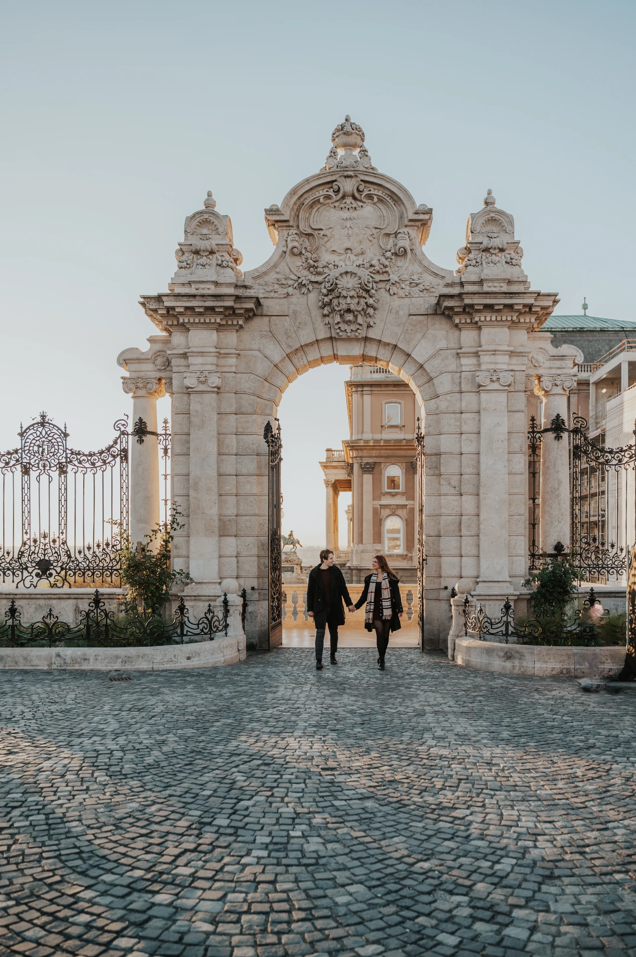 Couple standing hand in hand on the cobbled approach to the Buda Castle gate during their photoshoot in Budapest