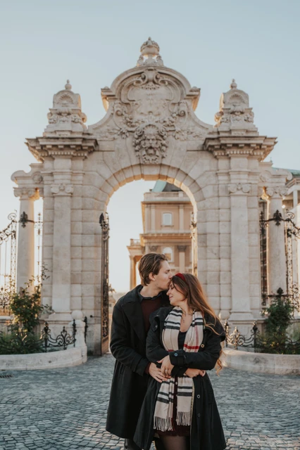 Budapest couple photoshoot with a forehead kiss by the castle gate Man kissing his partner on the forehead at the Buda Castle gate during their couple photoshoot in Budapest