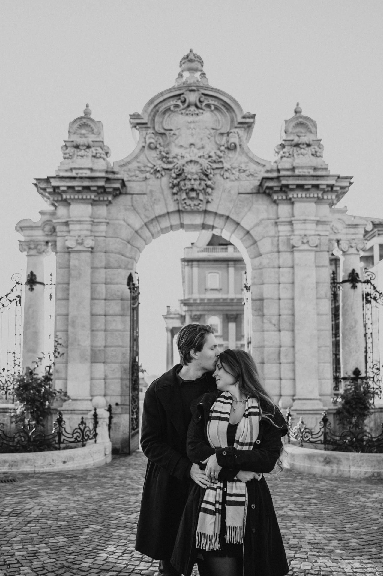 Black and white portrait of a forehead kiss at the Buda Castle gate during the couple's Budapest photoshoot