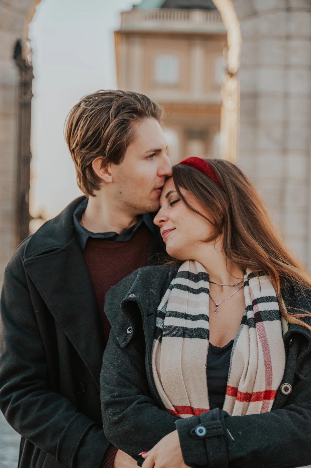 Close view of a forehead kiss during a morning couple photoshoot in Budapest, with the Buda Castle gate behind them