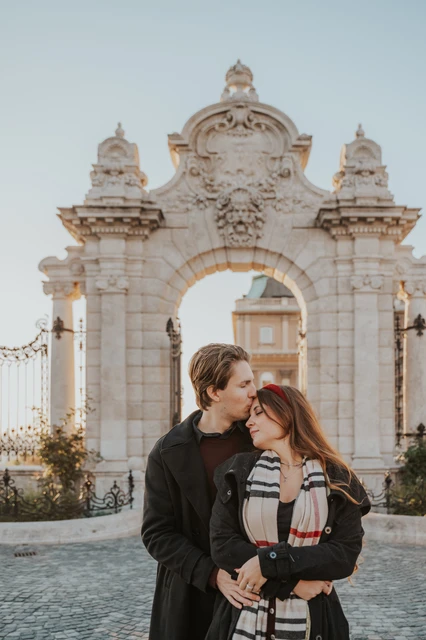 Couple photoshoot in Budapest with the castle gate in the backdrop Couple sharing a kiss on the cobbles in front of the Buda Castle gate during their Budapest photoshoot