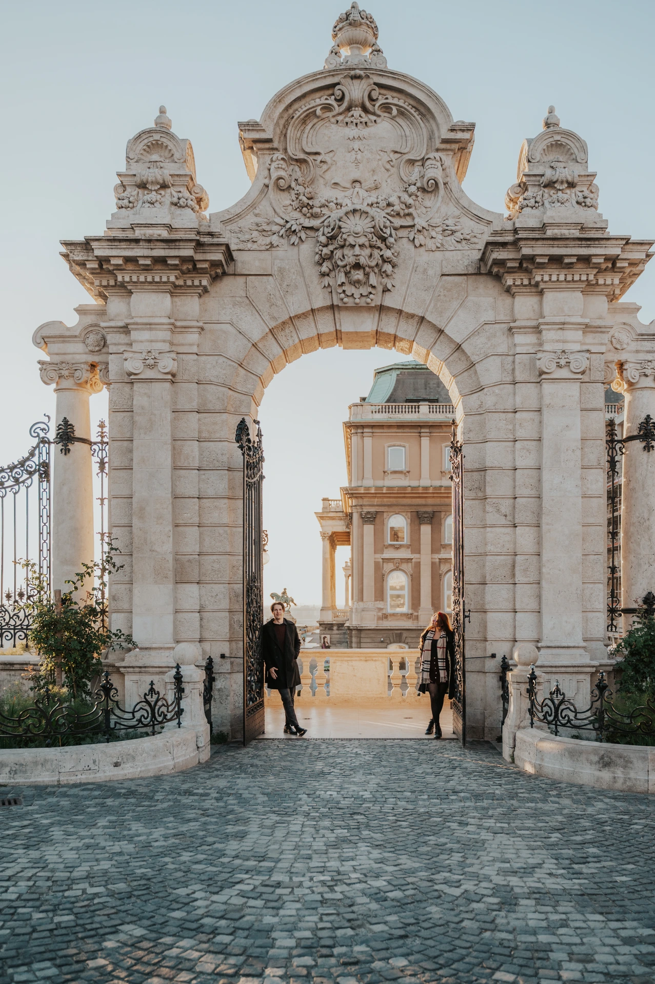 Couple standing close together beneath the stone arch of the Buda Castle gate during their photoshoot in Budapest