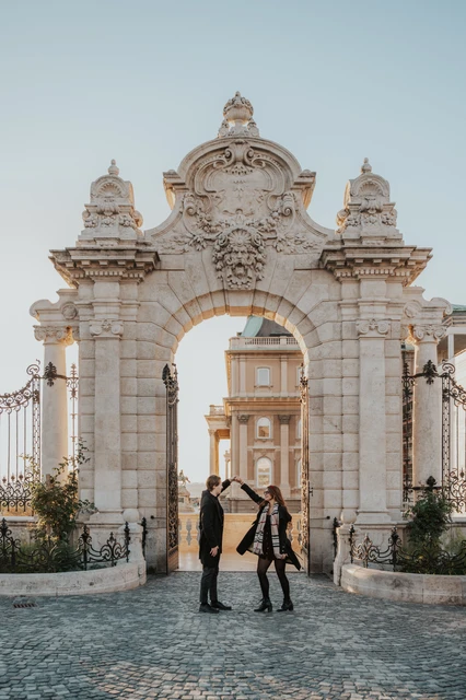 Couple photoshoot in Budapest with a turn beside the castle gate Man lifting their joined hands as his partner turns beside the Buda Castle gate during their couple photoshoot in Budapest
