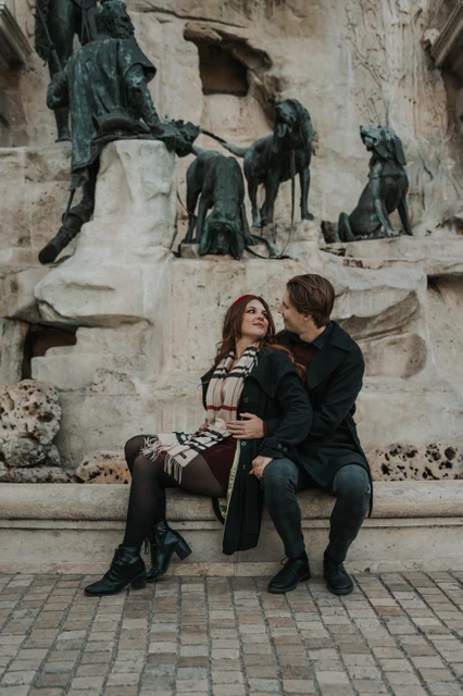Couple photoshoot in Budapest sitting beside the Buda Castle fountain Couple looking at each other on a bench beside the fountain sculptures at Buda Castle during their Budapest photoshoot